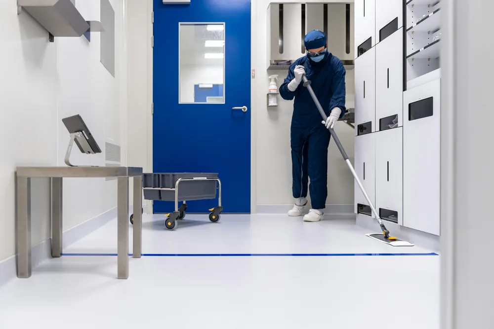 Cleaner in protective clothing mopping the floor of a bright, clinical commercial facility