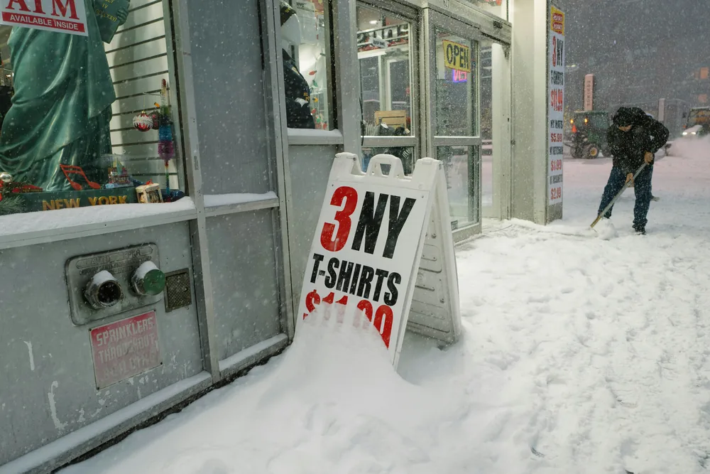 Worker shovelling snow from a storefront sidewalk during a snowstorm